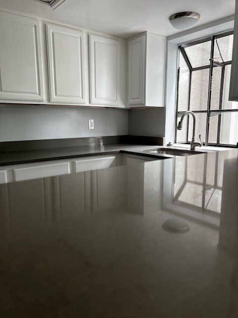 Empty modern kitchen with white cabinets, black countertops, and a large window beside a glossy island countertop