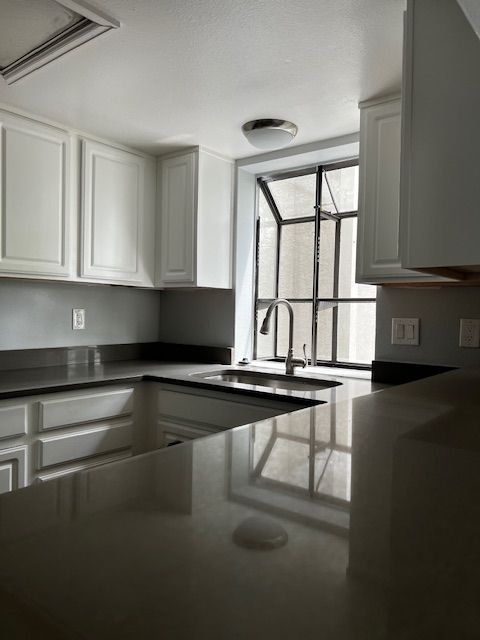Bright modern kitchen with white cabinets, dark countertops, and a window above the sink.