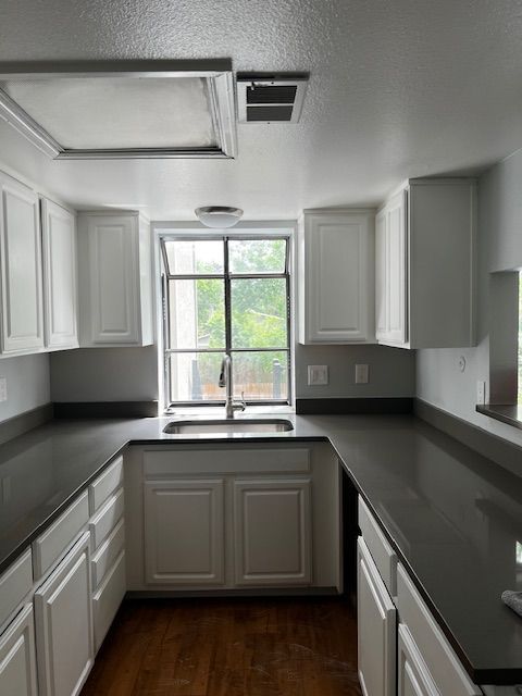 Modern white kitchen with gray countertops, cabinets, and a window over the sink looking out to greenery