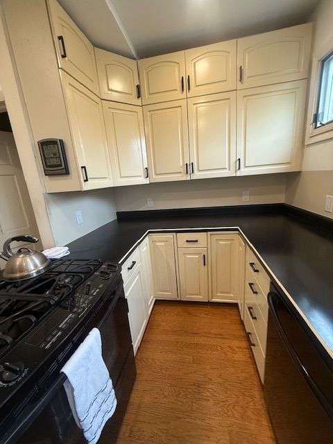Small galley kitchen with cream cabinets, black countertops, gas stove, and wood floor.
