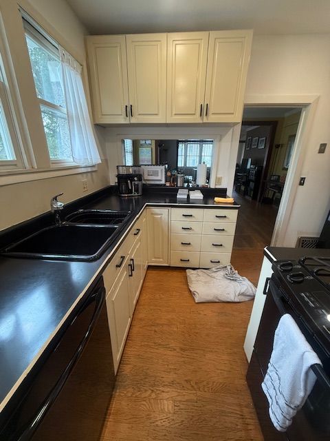 Small kitchen with white cabinets, black countertops, a window over the sink, and a towel on the floor.