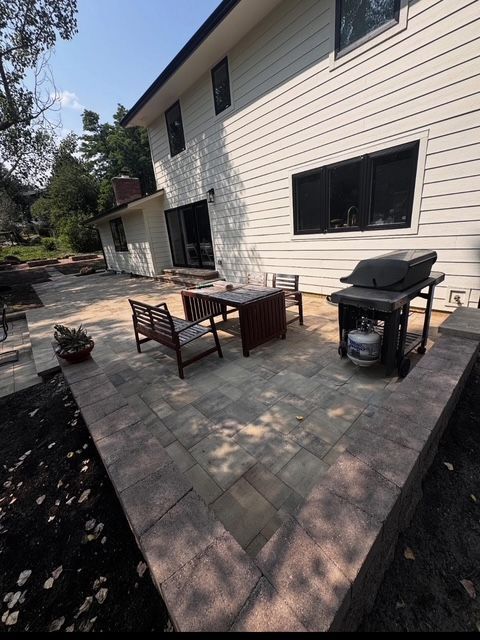Back patio with patio furniture, grill, and stone pavers beside a beige house