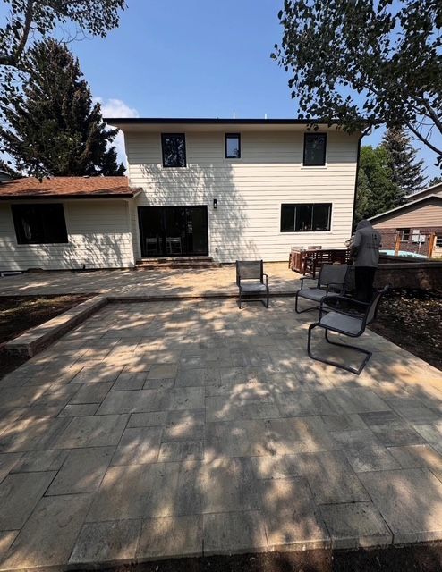 Backyard patio with stone pavers, outdoor chairs, and a two-story house in the background.