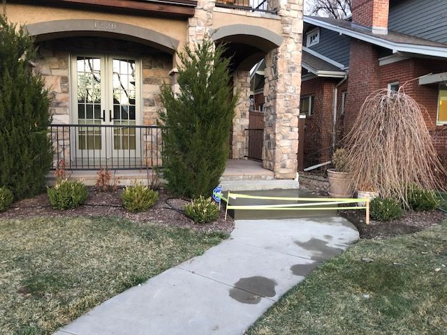 Front walkway with yellow caution tape leading to a brick house entrance, with damaged landscaping nearby