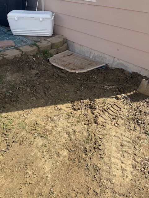 Backyard dirt patch by a house wall, with a small concrete step and white cooler near the corner.