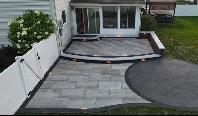 Backyard patio with gray pavers, curved steps, white fence, and sliding glass doors to the house