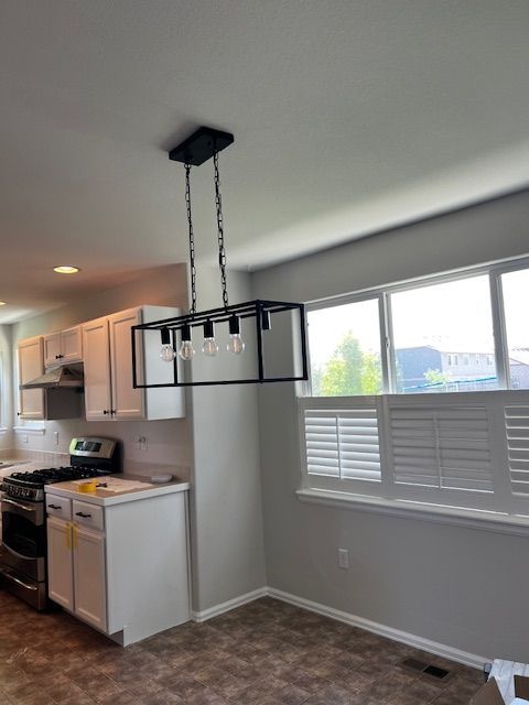Empty kitchen-dining area with white cabinets, gray walls, and a black rectangular pendant light over the table area