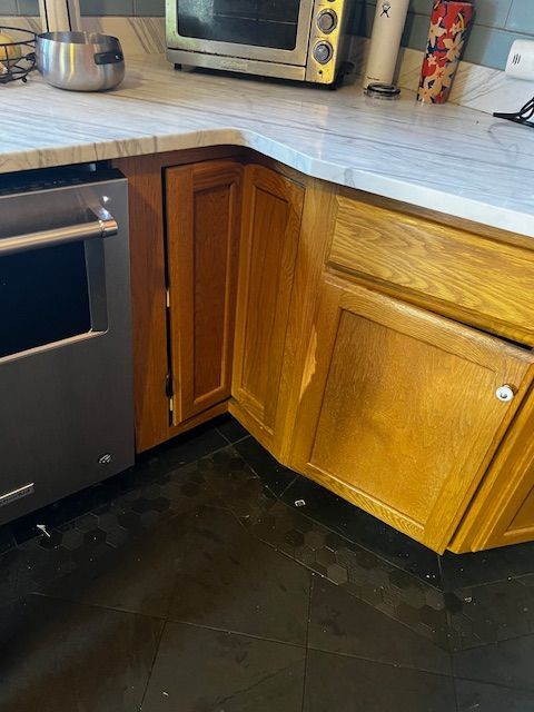 Kitchen corner with wooden cabinets, dark floor, and stainless-steel oven under a light countertop