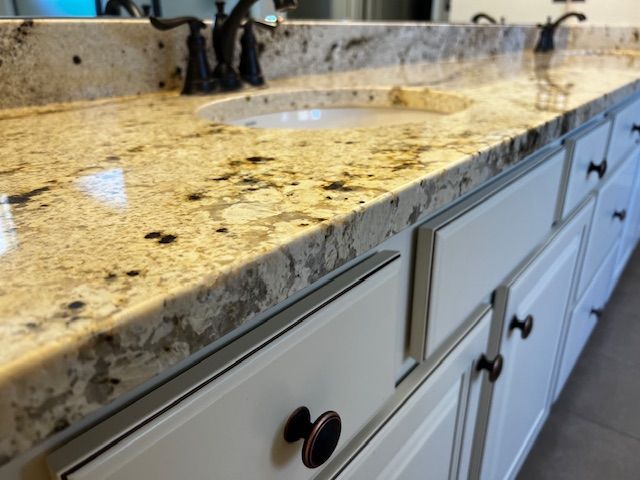 Dirty granite bathroom countertop with sink and white cabinets underneath