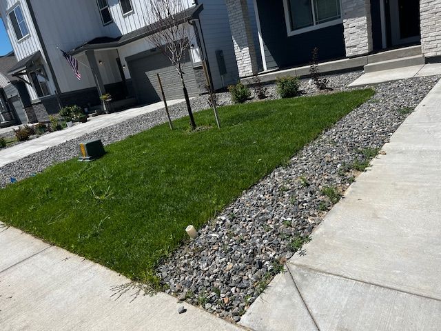 Sidewalks beside a small green lawn and gravel beds in front of modern apartment buildings.