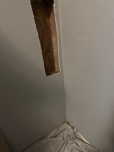 Damaged wall corner with a torn opening exposing wood and a wrinkled cloth at the base