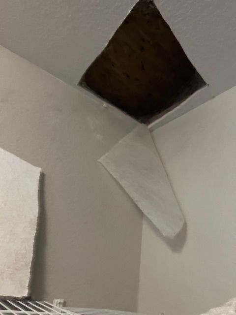 Damaged ceiling with a missing panel and a hanging white sheet in a corner room