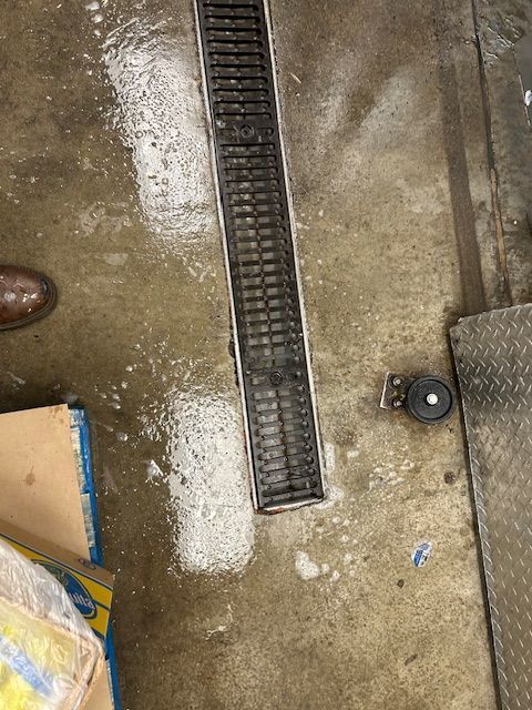 Wet concrete floor with a long black drainage channel and a small round floor fitting.