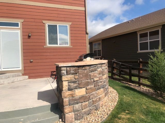 Stone planter beside a red house patio with a small yard and fence
