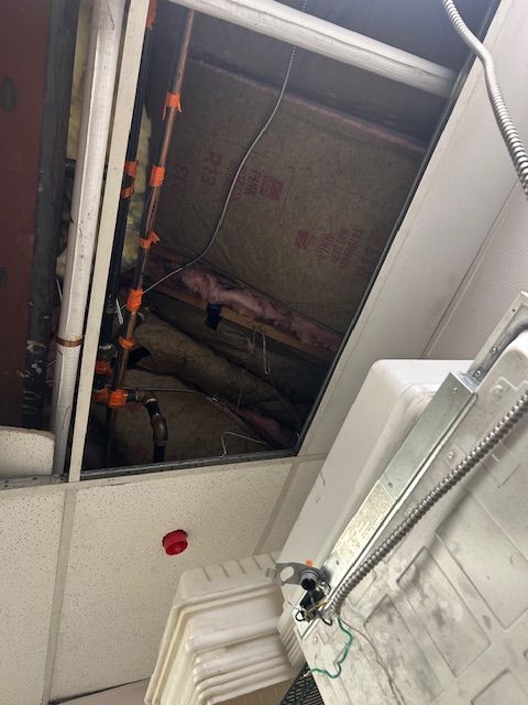 Open ceiling access panel showing ductwork, pipes, and wiring above a white wall.