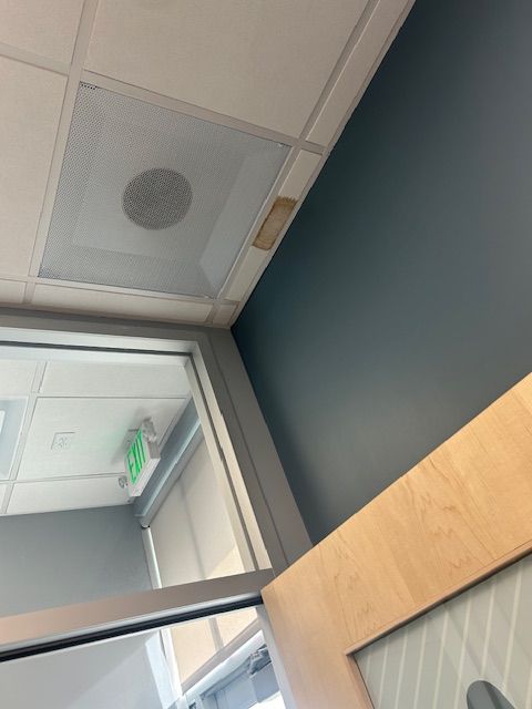 Tilted view of a hallway ceiling with white panels, a vent, teal wall, and wooden door frame