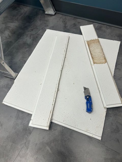 White boards and a blue utility knife on a gray floor, with one board showing a damaged patch.