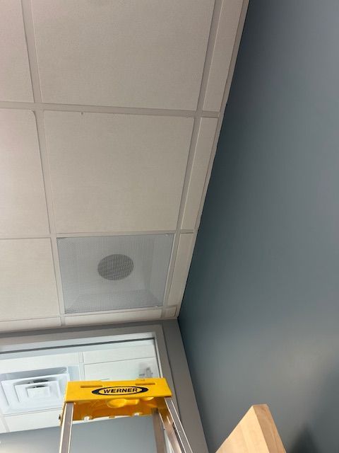 Yellow ladder under ceiling tiles next to a gray wall in a room