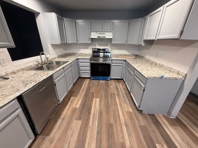 Modern U-shaped kitchen with gray cabinets, granite countertops, stainless appliances, and wood-look flooring.