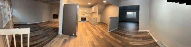 Empty modern living room with wood floors, gray fireplace, and staircase by a white railing.