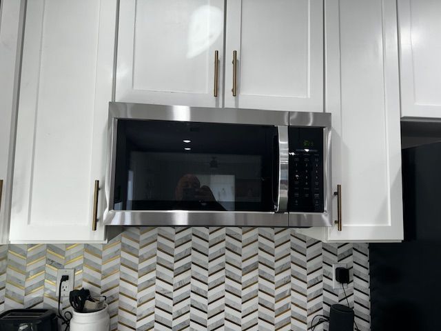 White kitchen cabinets with a stainless steel microwave above a chevron tile backsplash.