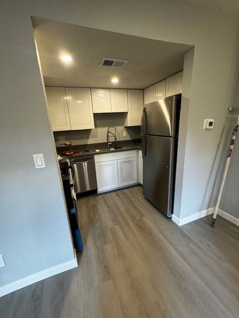 Compact kitchen with stainless steel appliances, white cabinets, and gray wood flooring viewed through an entryway