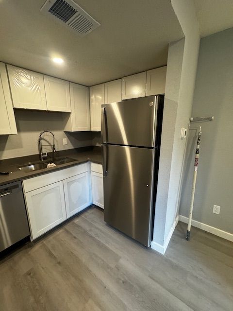 Compact kitchen with stainless steel fridge, white cabinets, dark countertops, and wood-look flooring.