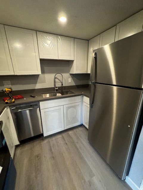 Small modern kitchen with white cabinets, stainless steel appliances, dark countertops, and light wood floor.