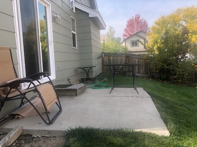 Backyard patio with a folding chair, small table, and grassy yard beside a house