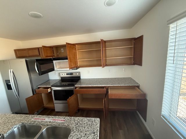 Empty kitchen with stainless steel appliances, wooden cabinets, and open shelving near a window