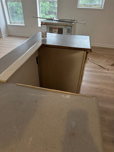 Renovation room with unfinished kitchen island, dust-covered floor, and windows in the background