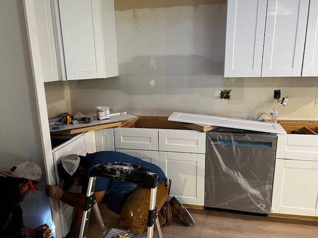 Kitchen under renovation with white cabinets, bare countertop, and a covered dishwasher.