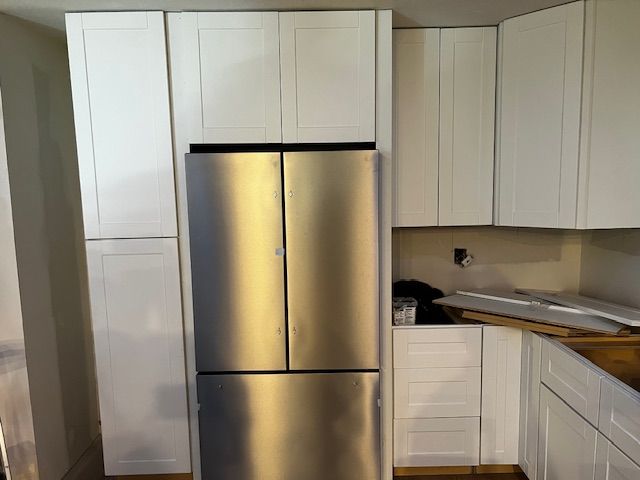 Modern kitchen with stainless steel fridge and white cabinets around a countertop and sink