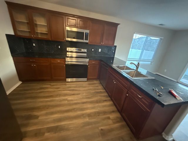 Empty modern kitchen with dark wood cabinets, black countertops, stainless appliances, and a window above the sink