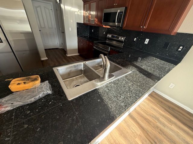 Modern kitchen with black granite counters, double sink, dark cabinets, and stainless steel appliances