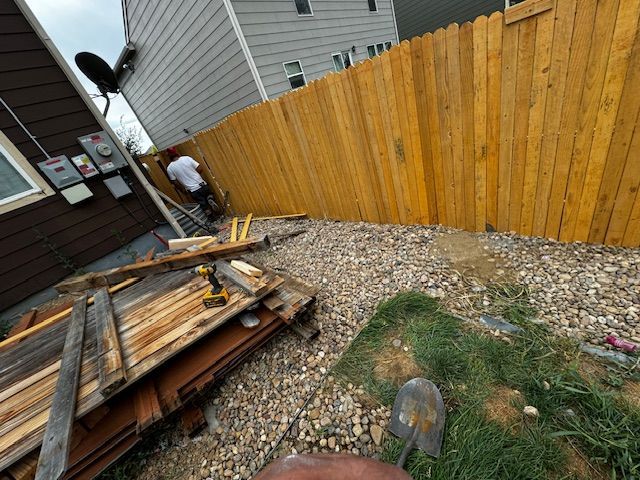 Person at the end of a narrow gravel alley beside a wooden fence and stacked construction materials