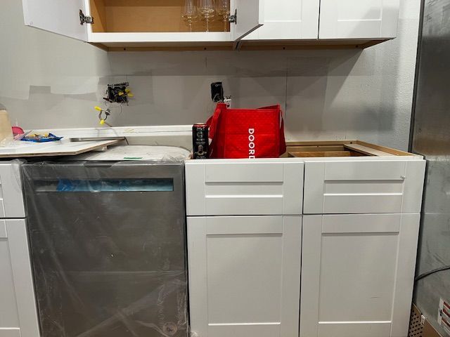 Small kitchen with white cabinets, gray dishwasher, and a red shopping bag on the counter