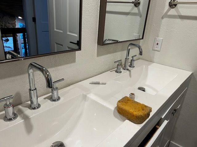 Double vanity bathroom sink with mirror, faucet, and a yellow sponge on the counter.