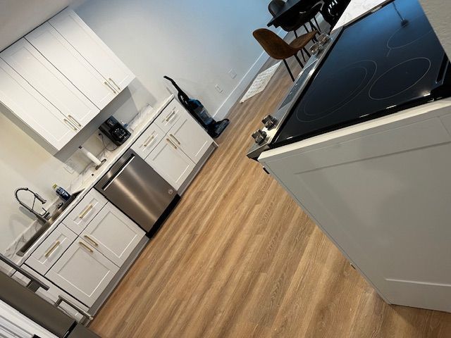 Modern kitchen with white cabinets, stainless dishwasher, wood floors, and a black glass cooktop.