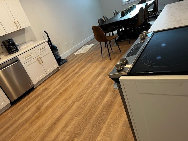 Modern kitchen and dining area with wood floors, white cabinets, black appliances, and a piano in the background