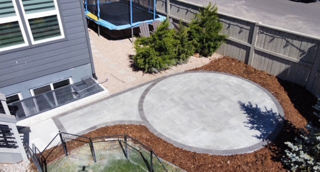 Backyard with a large round concrete patio, mulch border, small shrubs, and a house deck nearby