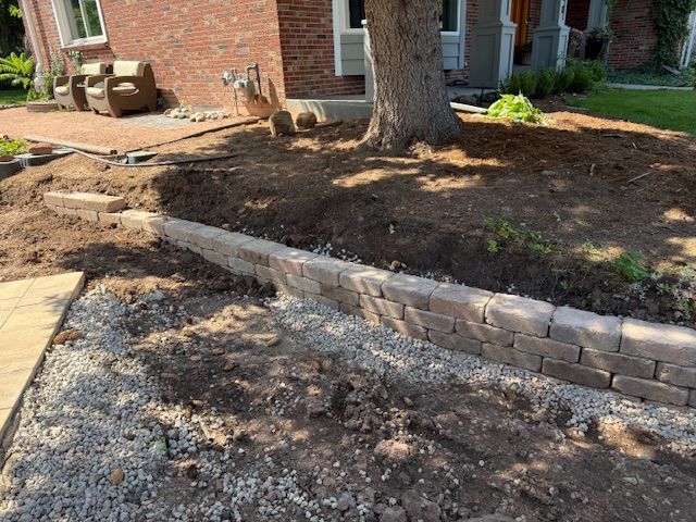 Front yard with a stone retaining wall, large tree, and mulched landscaping beside a brick house.