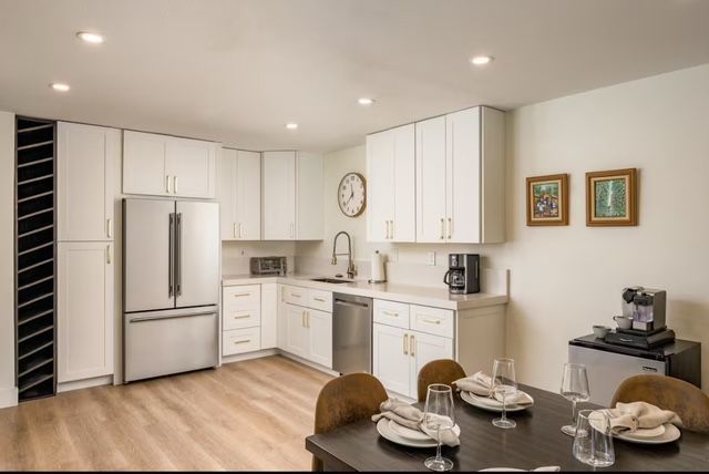 Bright modern kitchen and dining area with white cabinets, stainless fridge, and set table