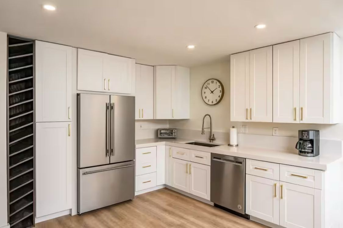 Bright modern kitchen with white cabinets, stainless appliances, wood floor, and wall clock
