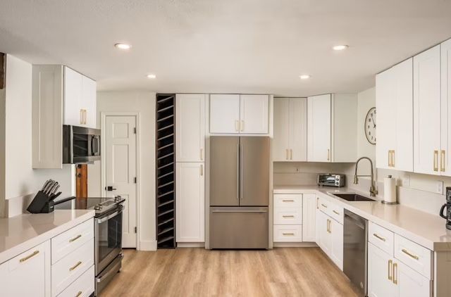 Bright modern kitchen with white cabinets, stainless steel appliances, and wood flooring