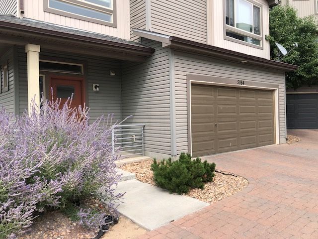 Townhouse exterior with tan garage, front steps, and purple flowering shrubs beside a brick driveway