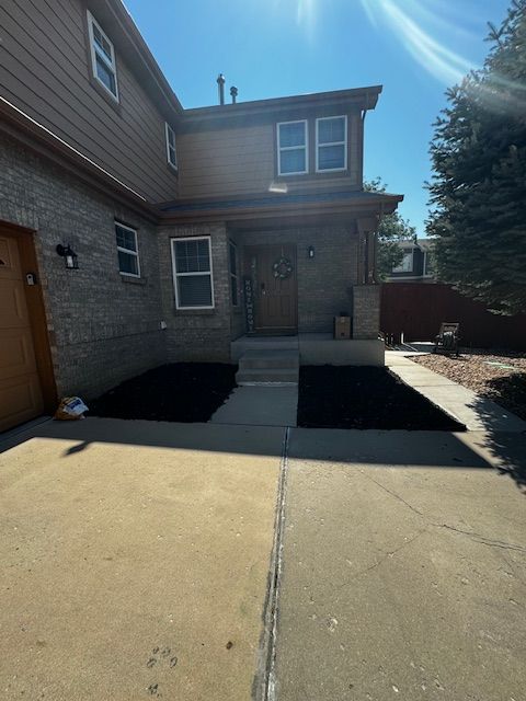 Front entrance of a brick townhouse with a concrete driveway, steps, and bright sunlight.
