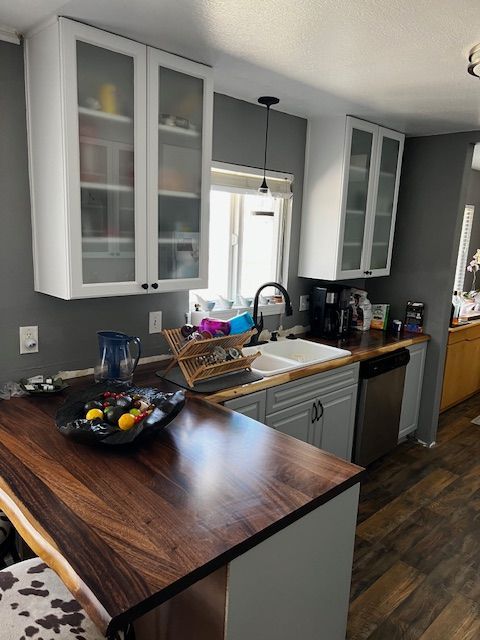 Modern kitchen with white cabinets, dark wood counters, and a sink by a window.