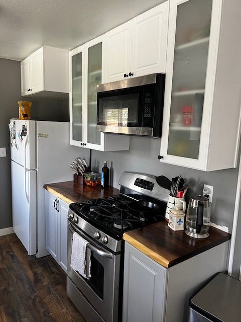 Compact white kitchen with stainless stove, microwave, fridge, and dark wood countertops