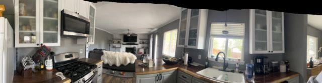 Modern kitchen and living room with gray walls, white cabinets, large windows, and couches by the TV